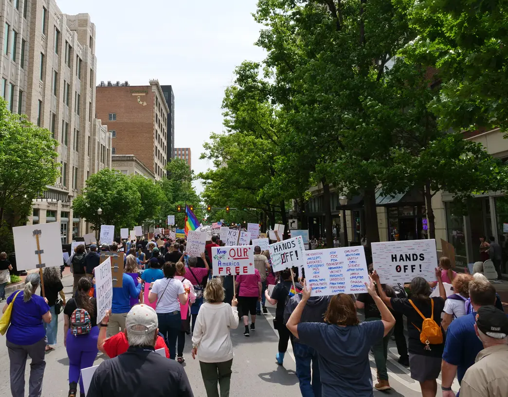Marchers filling a tree-lined downtown street, carrying handmade signs, photographed from behind the crowd.